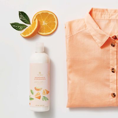 Thymes Mandarin Coriander Fabric Softener to Soften Fabric next to shirt and orange slice
